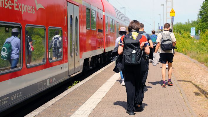 Fahrgäste laufen am Bahnhof neben einem Regionalexpress. (Quelle: dpa/Micha Korb)