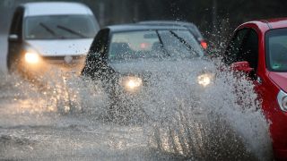 Autos fahren bei unwetterartigem Niederschlag über eine überflutete Straße. (Quelle: dpa/Ralf Hirschberger)