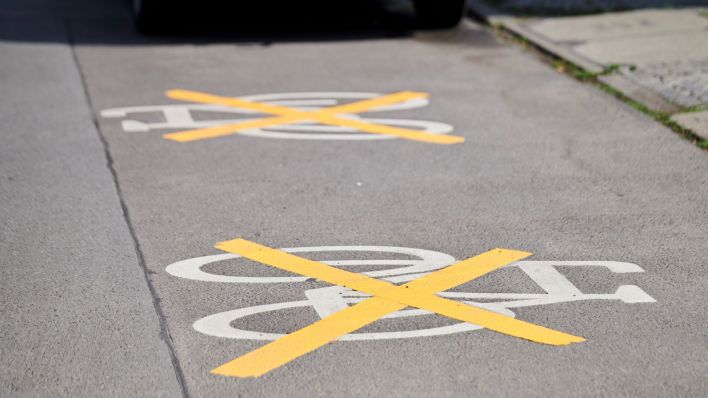 Auf der Ollenhauer Straße sind die Zeichen für den Radweg mit gelben Kreuzen zugeklebt und Autos parken darauf. Der Radweg existiert nicht mehr. (Quelle: Annette Riedl/dpa)