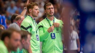 Füchse-Trainer Jaron Siewert berät sich mit seinem Co-Trainer während eines Spiels. Quelle: imago images/Eibner