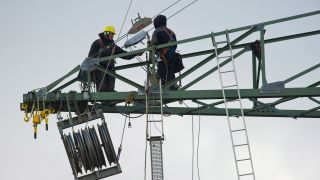 In circa 60 Metern Höhe klettern zwei Arbeiter auf den Streben eines neuen Strommasten unweit vom brandenburgischen Bernau (Brandenburg). (Quelle: dpa/P. Pleul)