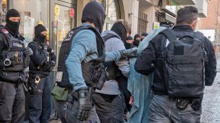 Ein Mann wird am 18.02.20231 bei einer Razzia in Berlin, mit einer Decke über dem Kopf, von der Polizei abgeführt. (Quelle: Picture Alliance/Christophe Gateau)