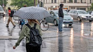 Eine Frau mit Regenschirm läuft am 27.06.2023 bei starken Regen in Berlin-Prenzlauer Berg über eine Kreuzung. (Quelle: Picture Alliance/Fabian Sommer)
