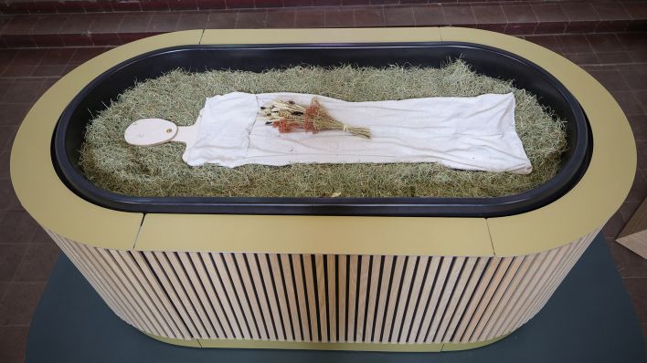 Heu, Stroh, Blumen und eine Holzfigur liegen in einem sogenannten „Kokon“ bei einem Pressegespräch zu der neuen Bestattungsform "Reerdigung" in der Kapelle auf dem Parkfriedhof Eichhof in Berlin. (Quelle: dpa/Christian Charisius)