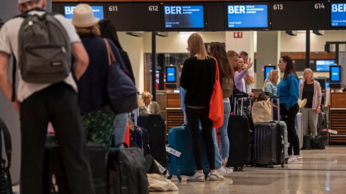 Symbolbild:Reisende stehen am Flughafen BER am frühen Morgen an einem Check-In-Schalter.(Quelle:dpa/P.Zinken)