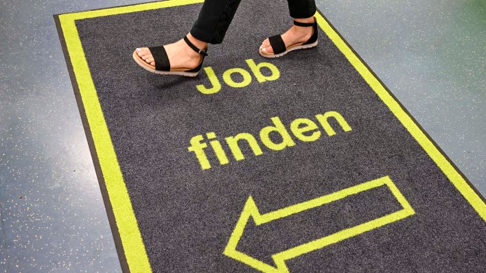 Symbolbild:Eine Frau geht im Jobcenter Berlin Charlottenburg-Wilmersdorf über einen Teppich mit der Aufschrift „Job finden“.(Quelle:dpa/J.Kalaene)