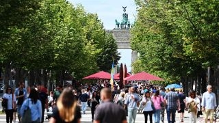 Symbolbild:Passanten gehen auf dem Mittelstreifen der Straße Unter den Linden vor der Kulisse des Brandenburger Tores.(Quelle:dpa/S.Stache)