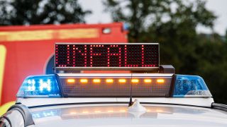 Symbolbild:Ein Polizeifahrzeug steht mit Blaulicht und dem Schriftzug Unfall im Display an einer Unfallstelle.(Quelle:picture alliance/Fotostand/Reiss)