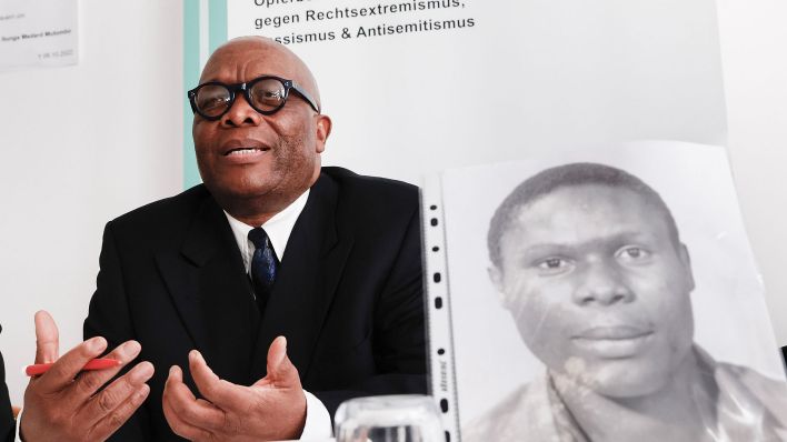 Archivbild: Mutombo Mansamba, sitzt hinter einem Bild seines gestorbenen Bruders Kupa Ilunga Medard Mutombo, bei einer Pressekonferenz in der Beratungsstelle ReachOut. (Quelle: dpa/C. Koall)