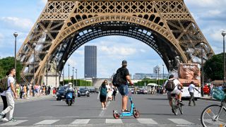 Symbolbild: Ein Mann fährt mit einem E-Scooter vor dem Eiffelturm in Paris auf der Straße. (Quelle: dpa/abaca)