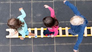 Drei Kinder balancierten auf dem Spielplatz einer Kita auf einem Spielgerät. (Quelle: dpa/Sebastian Kahnert)