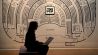 Eine Frau sitzt bei der Vorbesichtigung der Ausstellung "I've Seen the Wall" im "Das Minsk" Kunsthaus mit einem Laptop auf dem Schoß vor einem Foto von Evelyn Richter. (Quelle: dpa/Carla Benkö)