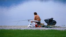 Symbolbild: Ein Angler sitzt oberköperfrei am See und Blickt aufs Wasser. (Quelle: dpa/Kirchner)