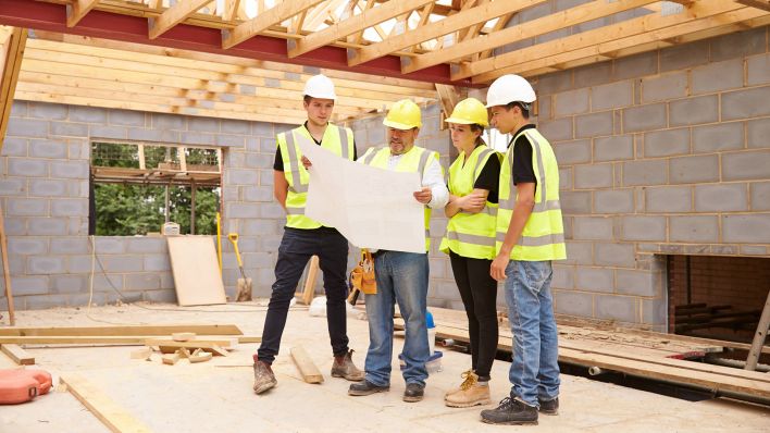 Symbolbild: Junge Erwachsene besprechen sich auf einer Baustelle mit ihrem Bauleiter. (Quelle: imago images/Monkey Business)