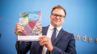 Carsten Schneider (SPD), Staatsminister und Ostbeauftragter der Bundesregierung, zeigt den Bericht zum Stand der Deutschen Einheit. (Quelle: dpa/Michael Kappeler)