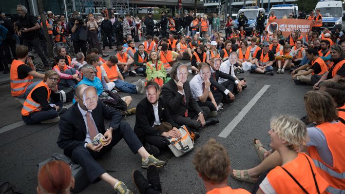 Demonstranten mit Scholz-Masken sitzen während eines Protestmarsches der Klimaschutzgruppe "Letzte Generation" vor dem Hauptbahnhof. (Quelle: dpa/S. Gollnow)