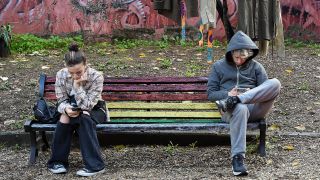 Symbolbild: Junge erwachsene sitzen gelangweilt auf einer Parkbank und schauen auf ihre Handydisplays. (Quelle: dpa/Zuma)