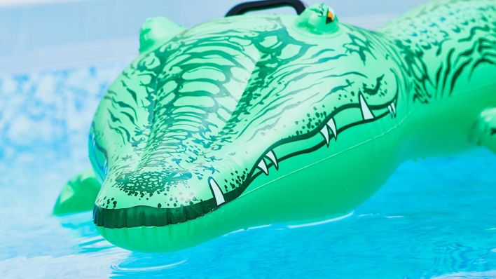Illustrtio: Ein aufblasbares grünes Spielzeug-Plastik-Krokodil in einem Pool. (Foto: picture alliance/Chromorange)