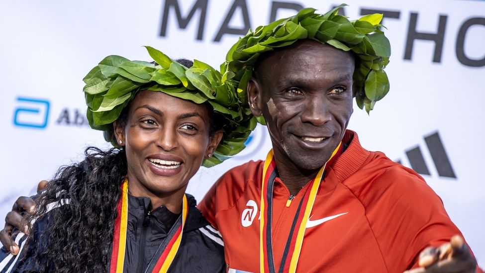 24.09.2023, Berlin-Marathon: Siegerin Tigst Assefa (l) aus Äthiopien steht lachend neben dem Sieger Eliud Kipchoge aus Kenia bei der Siegerehrung (Quelle: dpa/Andreas Gora).