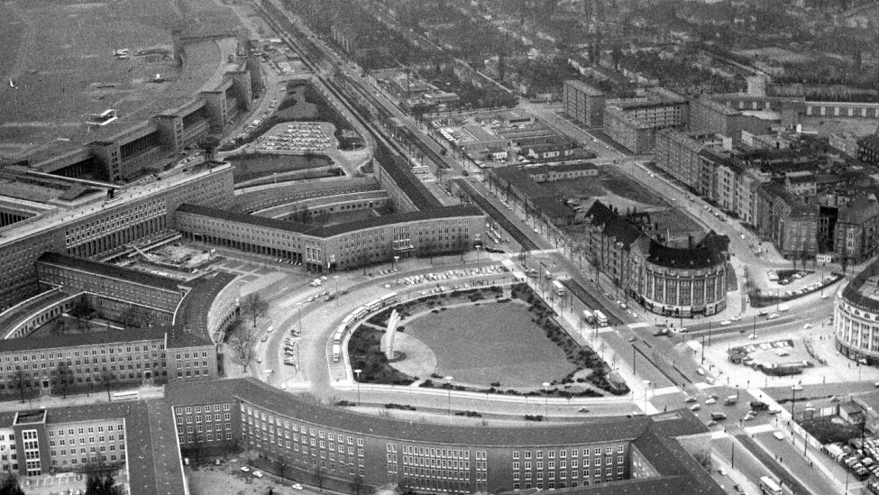 Blick auf die Bauten des Zentralflughafens Berlin-Tempelhof. Links oben ein Teil des Rollfeldes, in der Mitte das Luftbrücken-Denkmal für die während der Blockade ums Leben gekommenen Alliierten und Deutschen.