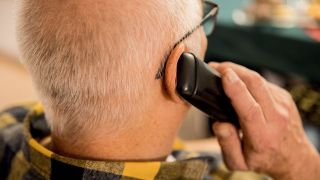Symbolbild: Ein älterer Menschen sitzt in seiner Wohnung und telefoniert mit einem Festnetztelefon. (Quelle: dpa/K. Schmitt)