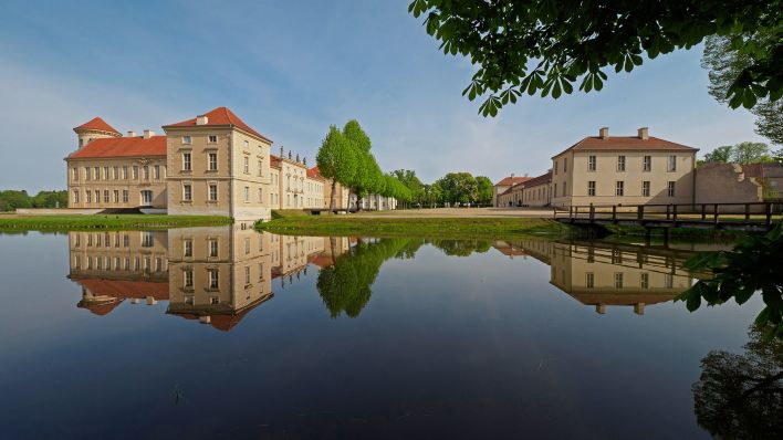Symbolbild: Die Parkseite von Schloss Rheinsberg und der Marstall (r) spiegeln sich in dem vom Grienericksee gespeisten Wasser des Schlossgrabens.(Quelle:dpa/S.Stache)