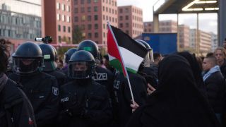 Polizisten (links) sind bei einer verbotenen Pro-Palästina-Demonstratin am Potsdamer Platz im Einsatz. Eine Frau hält dabei ein Palästinenser-Fähnchen. (Quelle: dpa/Paul Zinken)