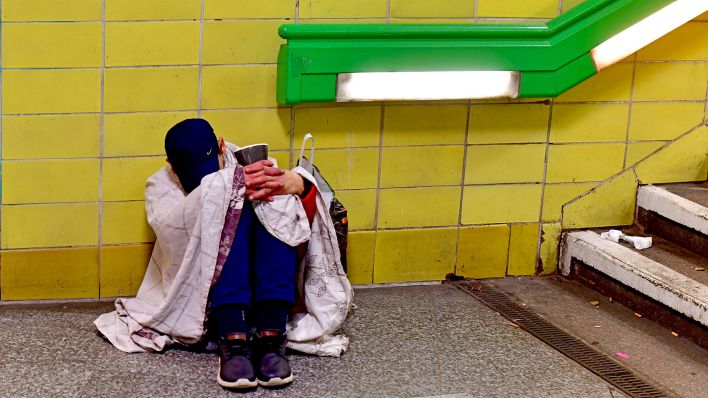 Obdachloser sitzt in eine Decke eingehüllt morgens im Bahnhof Tempelhof.