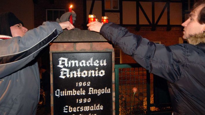 Archiv: Zwei Maenner stellen Kerzen ueber einer Gedenktafel fuer den Angolaner Amadeu Antonio in Eberswalde auf. (Foto: picture alliance / AP Photo)