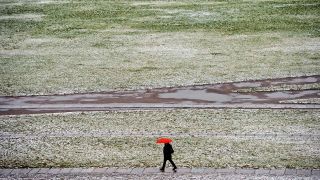 Symbolbild:Ein Mann mit rotem Regenschirm geht in Berlin über die mit wenig Schnee bedeckte Reichstagswiese.(Quelle:picture alliance/dpa/S.Stache)