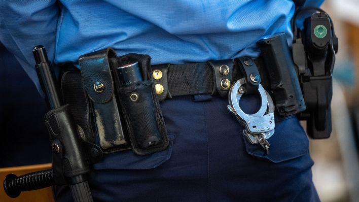 Handschellen und eine Dienstwaffe sind an dem Gürtel eines Polizisten befestigt (Quelle: dpa)