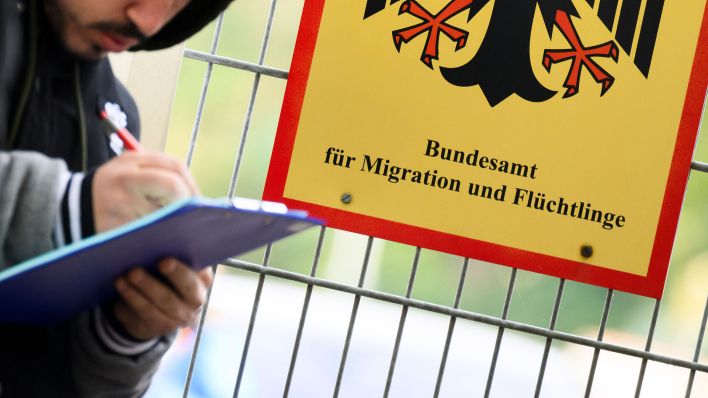 Ein Mann füllt ein Formular aus neben einem Schild vom Bundesamt für Migration und Flüchtlinge. (Quelle: dpa/Julian Stratenschulte)