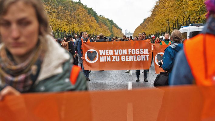 Umwelt-Aktivisten haben die Straße des 17. Juni besetzt und halten ein Plakat mit der Aufschrift "Weg von Fossil hin zu gerecht". (Quelle: dpa/Paul Zinken)