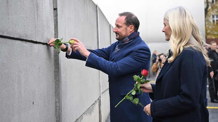 Der norwegische Kronprinz Haakon und seine Frau Kronprinzessin Mette-Marit stecken bei der Zentralen Gedenkveranstaltung des 34. Jahrestags des Mauerfalls an der Gedenkstätte Berliner Mauer Rosen in die Mauer. (Quelle: dpa/Britta Pedersen)