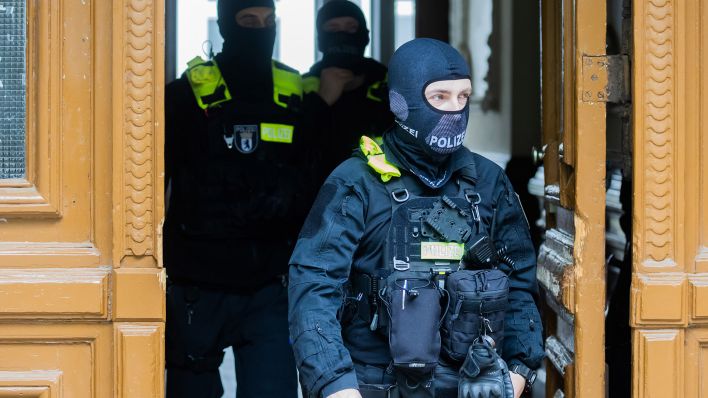 Symbolbild: Polizisten kommen bei einer Hausdurchsuchung in Berlin-Kreuzberg aus einem Gebäude. (Quelle: dpa/C. Soeder)