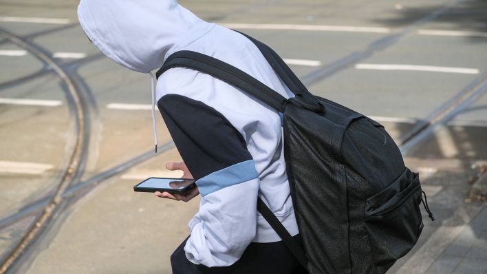 Symbolbild: Ein Jugendlicher geht mit seinem Smartphone am 25.09.2023 über eine Straße in Düsseldorf. (Quelle: Imago Images/Michael Gstettenbauer)
