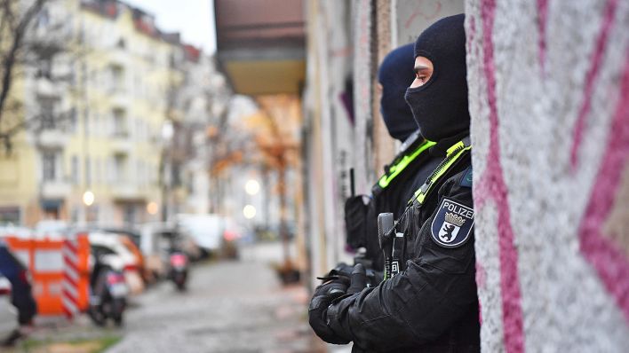 Polizeibeamte stehen am 23.11.2023 bei einer Razzia in Berlin-Friedrichshain am Eingang eines Gebäudes. (Quelle: dpa-Bildfunk/Paul Zinken)