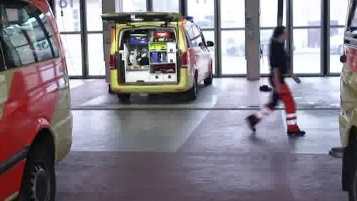 Parkplatz mit einer Person die nach rechts läuft. Ein Notruffahrzeug ist von hinten zu sehen mit offener Heckklappe (Quelle: rbb)