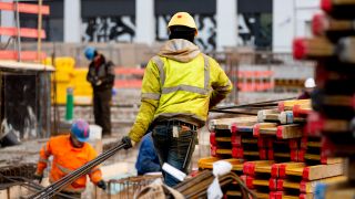 Symbolbild:Ein Bauarbeiter trägt auf einer Baustelle nahe des Alexanderplatzes Stahlstangen.(Quelle:picture alliance/dpa/C.Soeder)