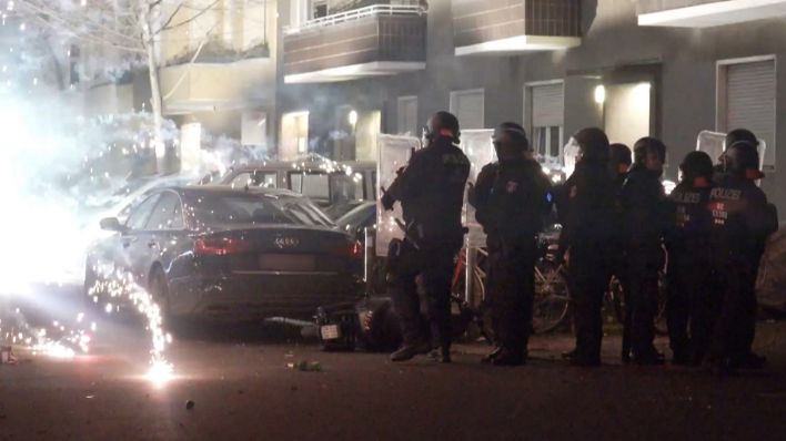 Polizisten stehen in der Silvesternacht 2022 in einer Straße, in der Nähe explodiert Feuerwerk. Bild: picture alliance/TNN, Schreiner