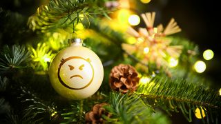Symbolbild: Weihnachtskugel mit Wut-Emoji hängt an einem Weihnachtsbaum,