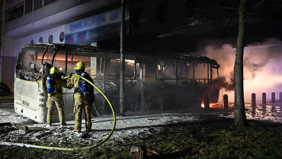 Feuerwehrleute löschen in der Silvesternacht am 01.01.2023 an der Sonnenallee im Bezirk Neukölln einen brennenden Bus, der von Randalierern angezündet wurde. (Quelle: dpa-Bildfunk/Paul Zinken)