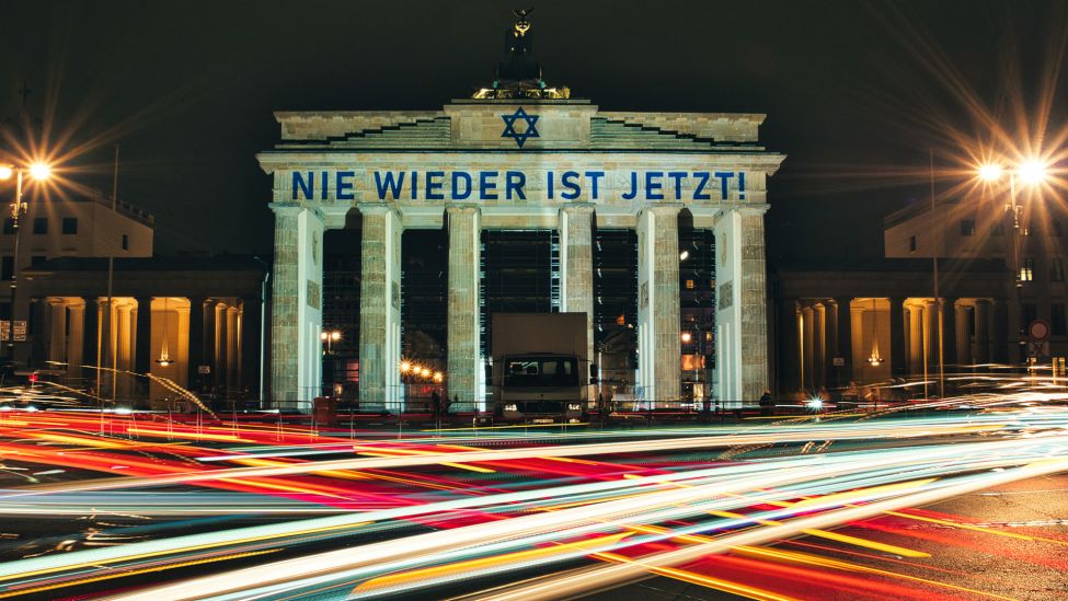 Der Schriftzug «Nie wieder ist jetzt» wird zum 85. Jahrestag der Pogromnacht am 09.11.2023 an das Brandenburger Tor projiziert (Quelle: dpa / Paul Zinken).