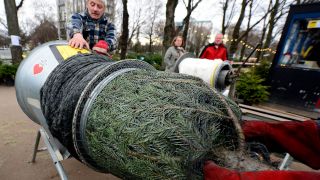 Symbolbild: Ein Verkäufer schiebt einen Weihnachtsbaum durch ein Rohr, um ihn für den Kunden in einem Netz zu verpacken. (Quelle: dpa/Steffen)