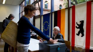 Symbolbild: Eine junge Frau steckt am Sonntag in einem Kreuzberger Wahllokal in der Wrangelstraße in Berlin die gefalteten Stimmzettel für die Wahl in die Urne. (Quelle: dpa/Stache)