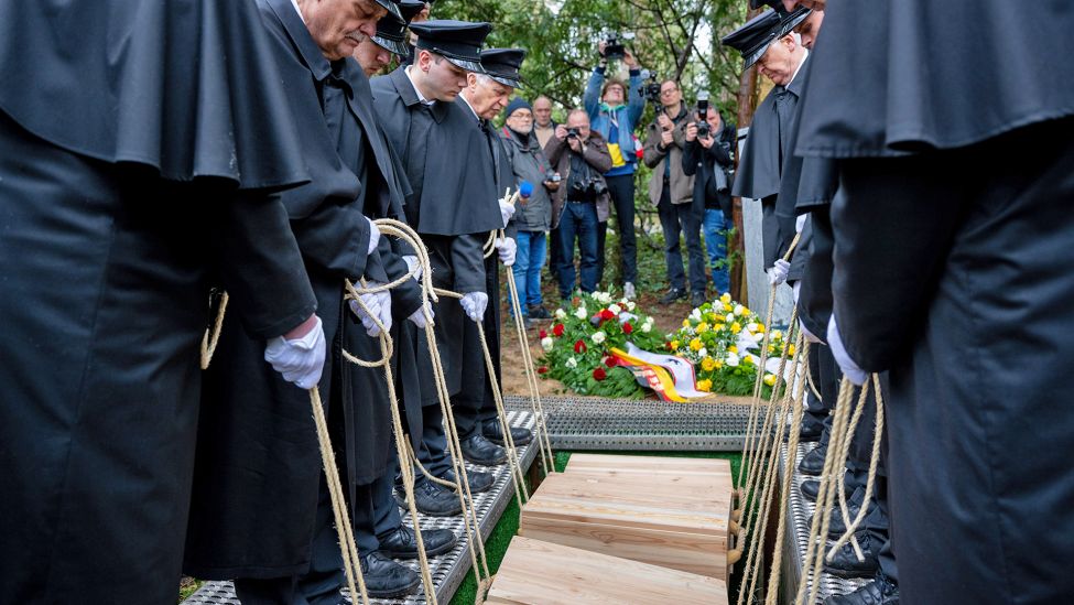 Gebeinekisten mit menschlichen Knochen werden nach der Trauerfeier in ein Grab auf dem Waldfriedhof Dahlem hinabgelassen.