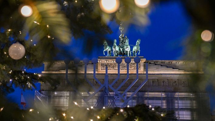 Ein Blick durch die 23 Meter hohe beleuchtete Tanne aus Ostthüringen auf dem Pariser Platz zeigt das Brandenburger Tor mit der Quadriga. Davor ist ein Teil des Chanukka-Leuchters zu sehen (Quelle: dpa/Jens Kalaene).
