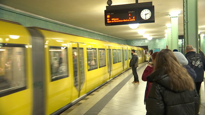 S-Bahn fährt in den Bahnhof, Menschen warten auf dem Bahnsteig.