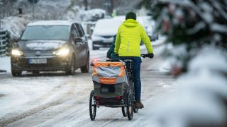 Symbolbild:Ein Fahrradfahrer ist mit einem Anhänger auf einer verschneiten Straße unterwegs.(Quelle:picture alliance/dpa/R.Hirschberger)