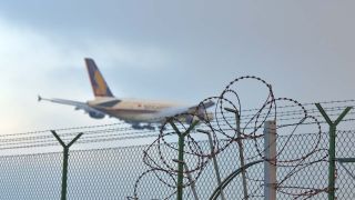 Symbolbild: "Abschiebeflug" - Ein Flugzeug hebt ab, im Vordergrund ist ein Zaun mit Stacheldraht zu sehen. (Quelle: dpa/Kubirski)